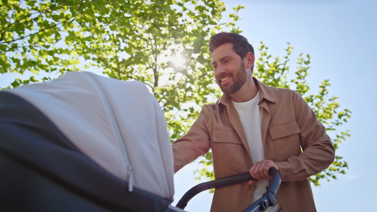 Single father walking baby carrying stroller crossing at sunny alley closeup