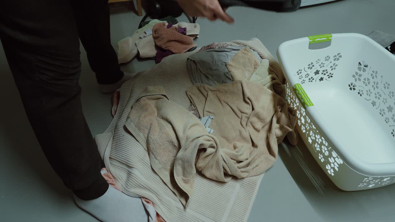 Person separating clothes by color on the floor next to a laundry basket, demonstrating proper washing preparation, fabric care and household organization