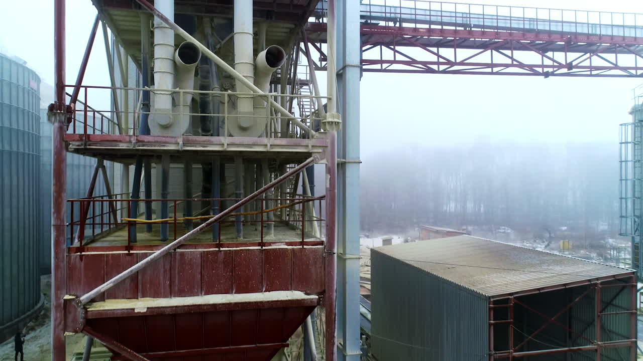 Metal supports, ladders and pipes at the tanks of modern silo plant. Rising along the massive metal construction of elevator. Foggy background.