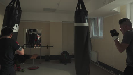 fighters exercise with punching bags in public gym. martial arts sportsmen team trains attack and defence in sports club slow motion. combat techniques