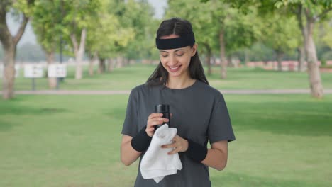 Happy-Indian-girl-wiping-sweat-and-drinking-water-after-workout