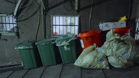 trash bags and rectangular trash cans on slanted roadway outside of building with exposed wires