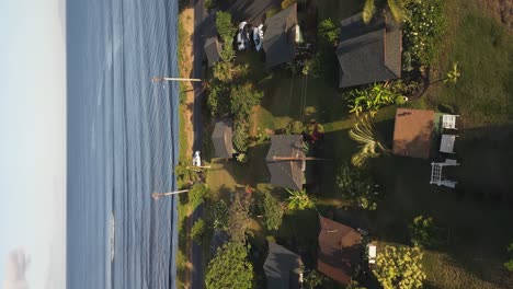 vertical format aerial rotates over beach front bungalow houses on maui