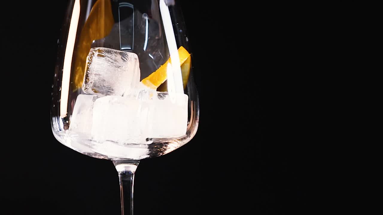 Close-up of ice cubes and an orange slice in a clear glass against a black background.