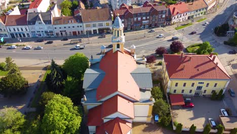 City-of-Kapuvar-church-with-bell-tower-and-city-street-in-background,-aerial-drone-view