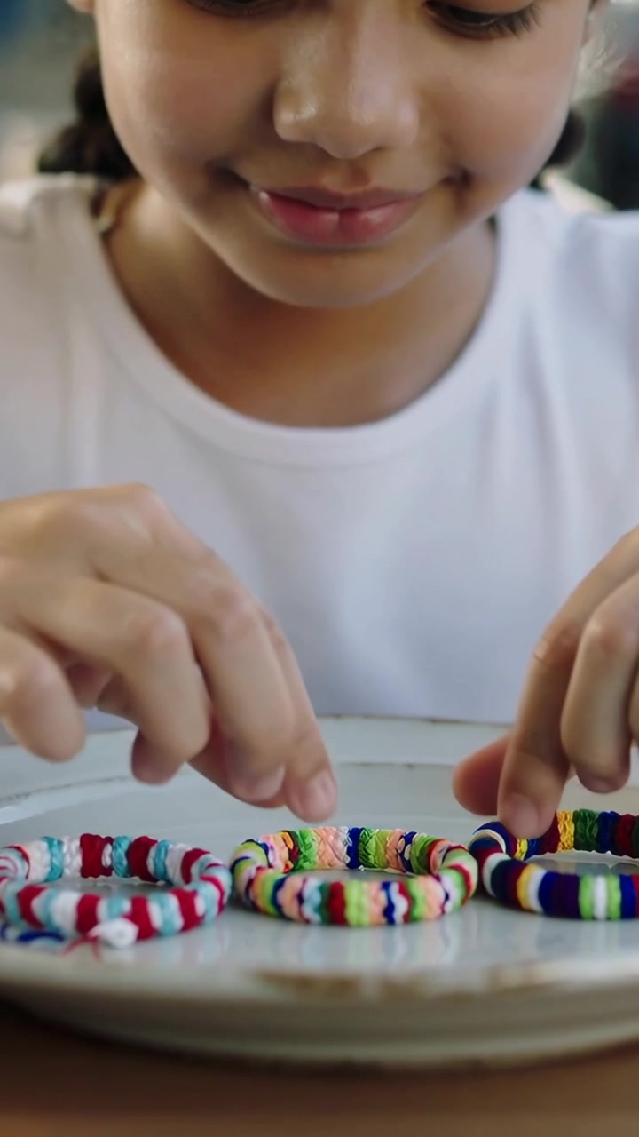 Vertical video: Spotting bracelets, child with braids touching and aligning them on plate at table