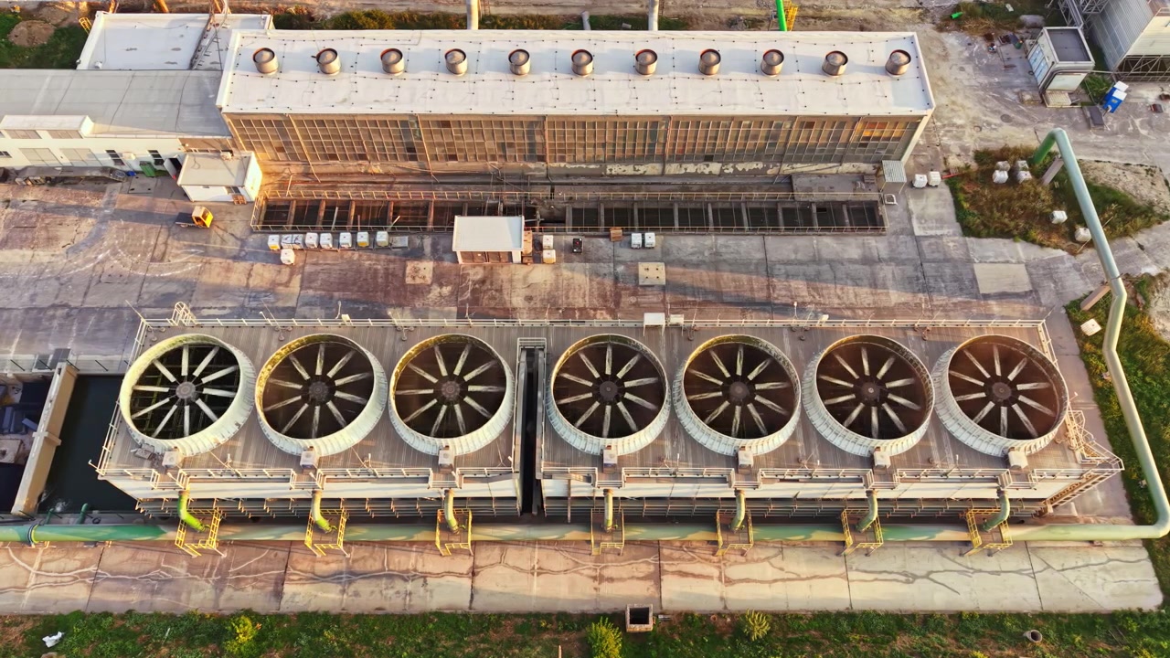 Industrial site with cooling towers and large fans viewed from above during daylight