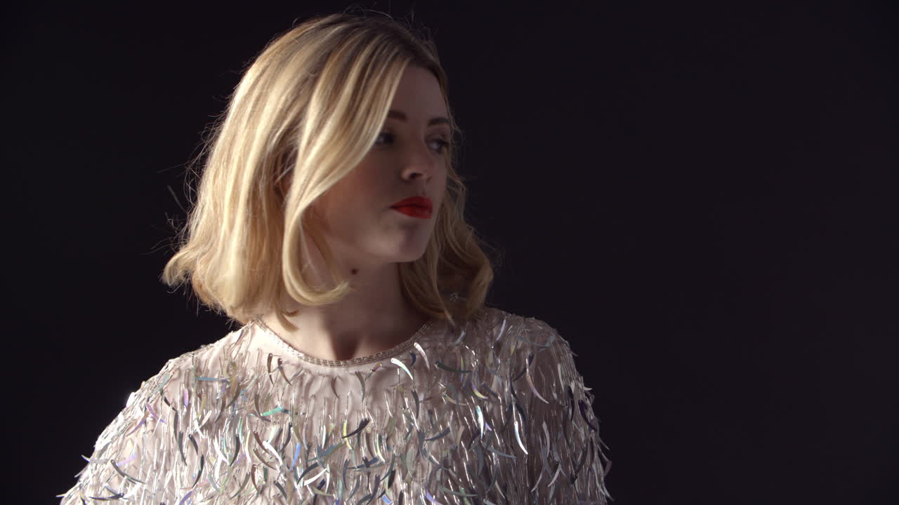 화려한 금발 여성이 카메라로 돌아서고, 가까이 다가갑니다.