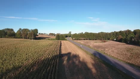 Quad-Bike-Driving-on-a-Field-Next-to-a-Road-on-a-Sunny-Autumn-Afternoon-in-South-Sweden-Skåne-Österlen,-Aerial-Descending-Following-Shot