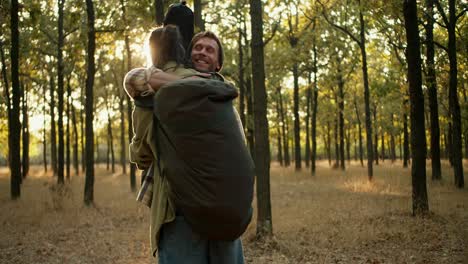 2-happy-friends-met-while-hiking.-A-brunette-man-in-a-light-green-jacket-with-a-large-hiking-backpack-and-a-blond-man-in-a-hat-in-a-checkered-shirt-come-to-each-other-and-hug-against-the-backdrop-of-a-summer-forest-and-continue-their-journey-on-a-hike