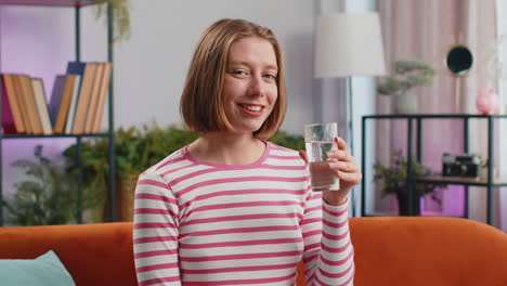 Thirsty-young-woman-sitting-at-home-holding-glass-of-natural-aqua-make-sips-drinking-still-water