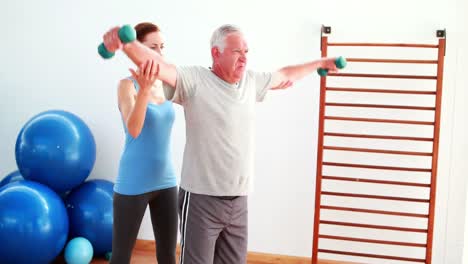 hombre mayor levantando pesas de mano con la ayuda de su entrenador