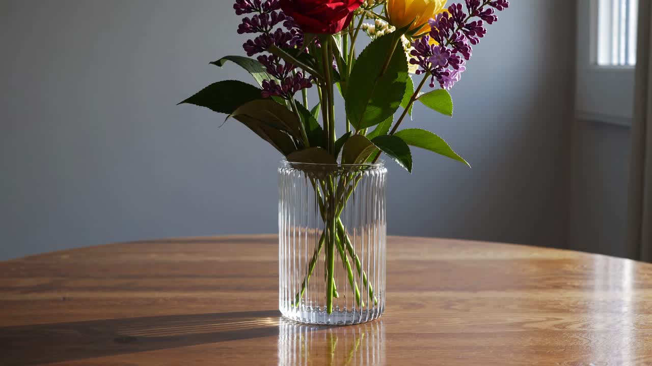 Vídeo estético de un arreglo floral en un jarrón de cristal sobre una mesa de madera