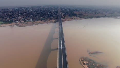 Flying-over-the-Benue-River-bridge-in-Makurdi-Town,-West-Africa-with-the-smoggy-city-skyline-on-the-horizon