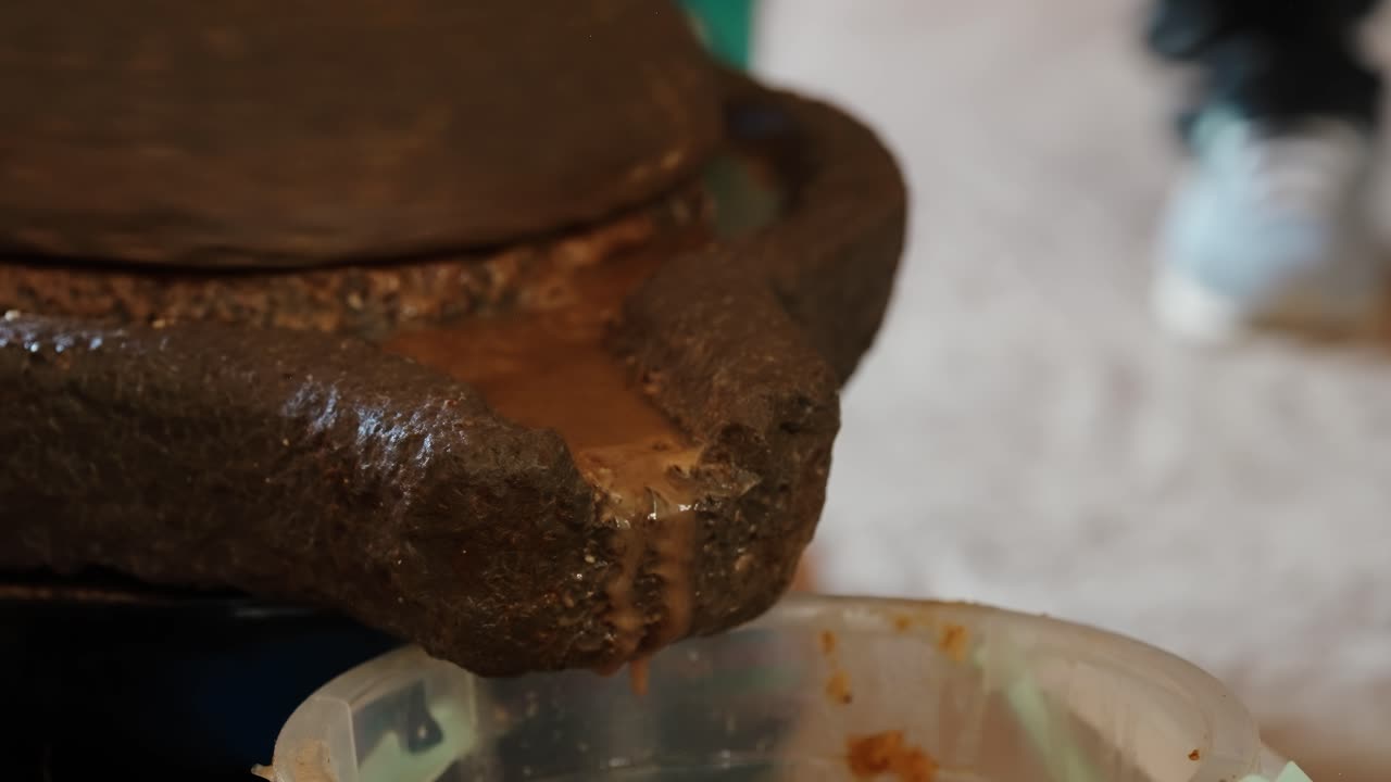Pasta di Argan che esce da una macina di pietra tradizionale in un contenitore in un mercato marocchino