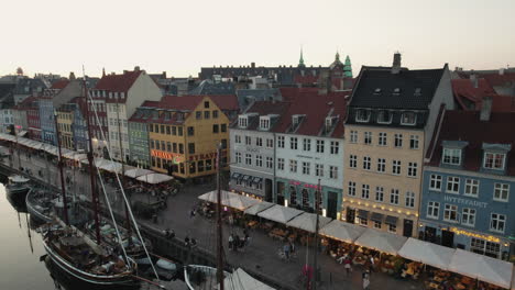 Nyhavn-En-Copenhague-Durante-La-Puesta-De-Sol,-Creando-Una-Atmósfera-Cálida-Y-Acogedora-Con-Gente-Y-Barcos-Bordeando-El-Canal