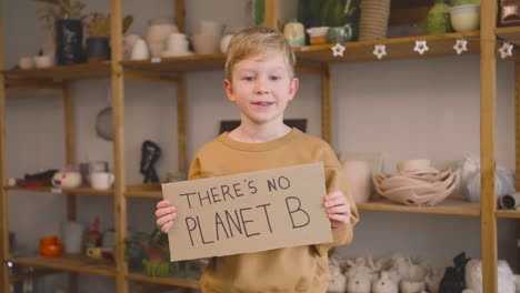 Blond-Kid-In-Craft-Workshop-Holding-A-Cardboard-Sign-With-There's-No-Planet-B-Phrase