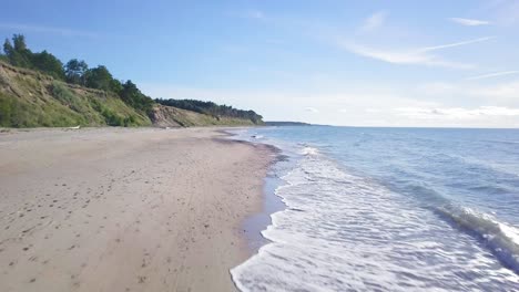 Aerial-view-of-Baltic-sea-beach-at-Jurkalne-on-a-sunny-day,-white-sand-cliff-damaged-by-waves,-coastal-erosion,-climate-changes,-wide-angle-drone-shot-moving-forward-low