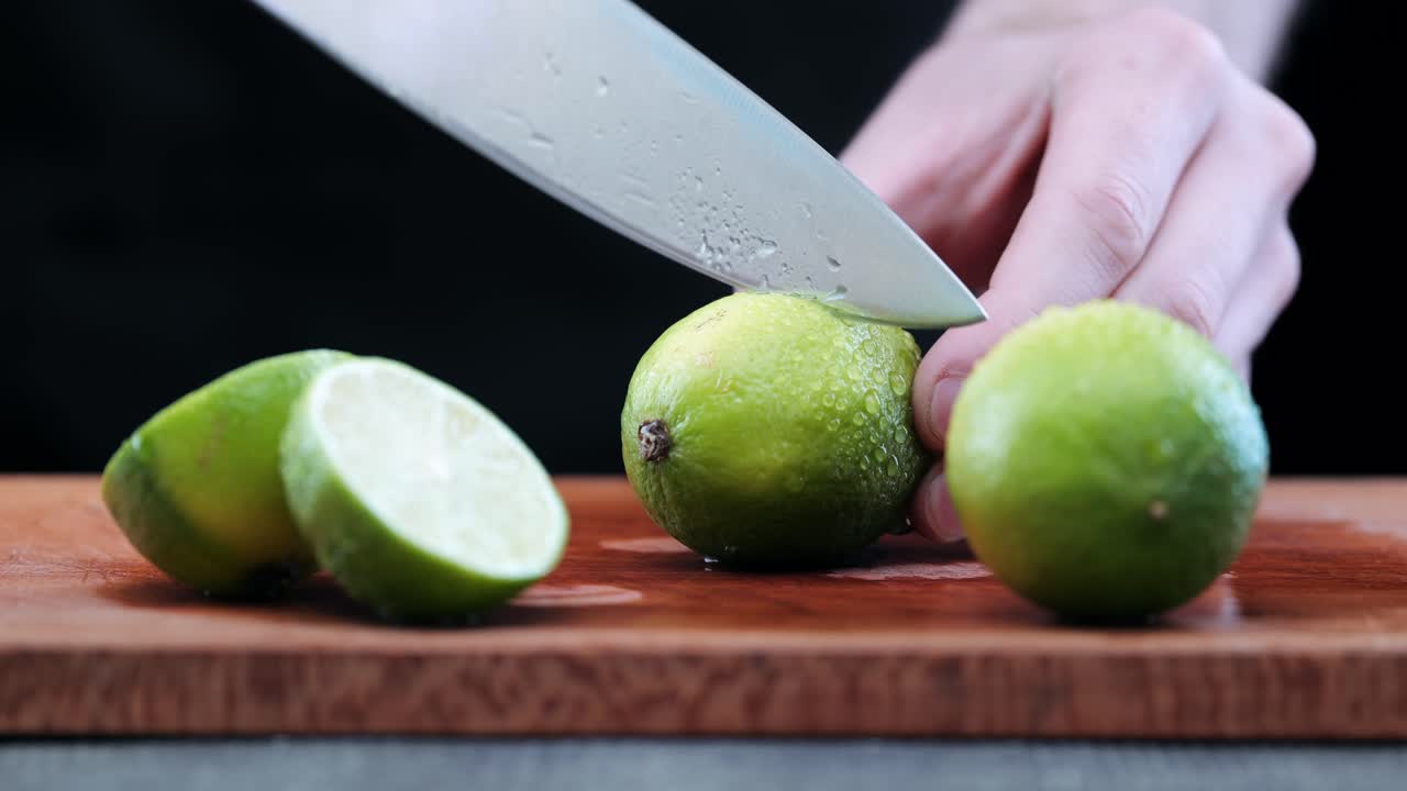 el chef con un cuchillo afilado corta limón verde fresco en una tabla de corte de madera