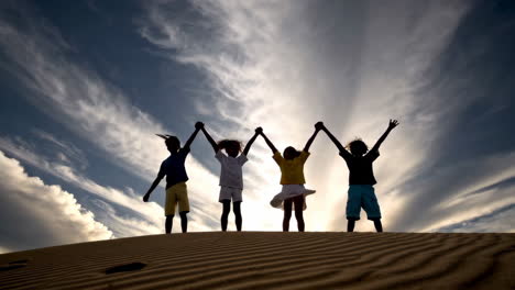 children silhouettes celebrating on a sand dune