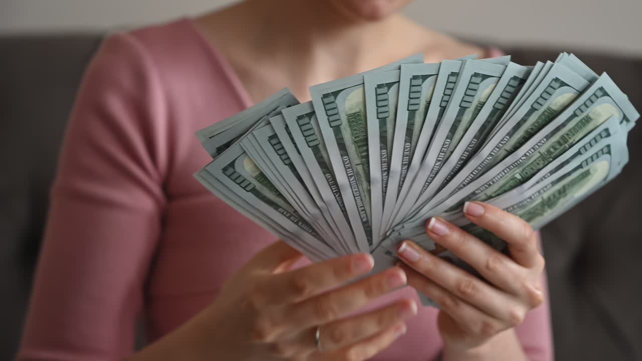 Smiling woman admiring a large fan of one hundred dollar bills in her hands