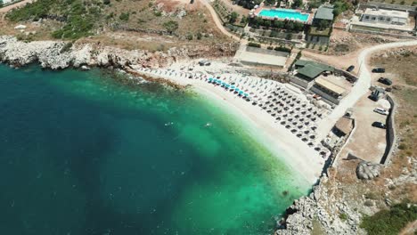 Albania,-blue-waters-of-the-Ionian-Sea,-pebble-beach-with-umbrellas-and-sunbeds