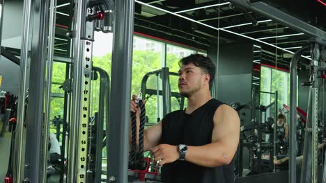a young man in athletic wear executes a tricep rope pushdown on a cable pulley machine in a well-lit, contemporary fitness center with mirrored walls