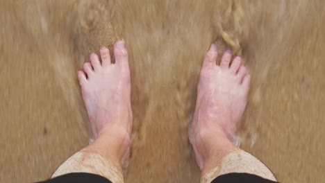 sea waves washing over male feet, young indian man standing on seashore and enjoying tides of sea on trip, guy enjoying summer vacation at seaside