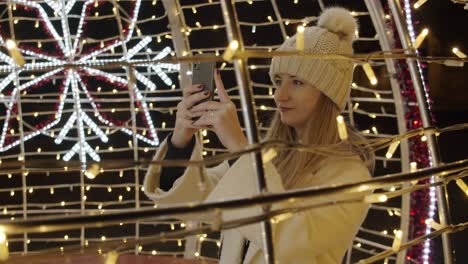 Mujer-Fotografiando-Coloridas-Decoraciones-Navideñas-Hechas-De-Luces-Con-Un-Teléfono-Por-La-Noche