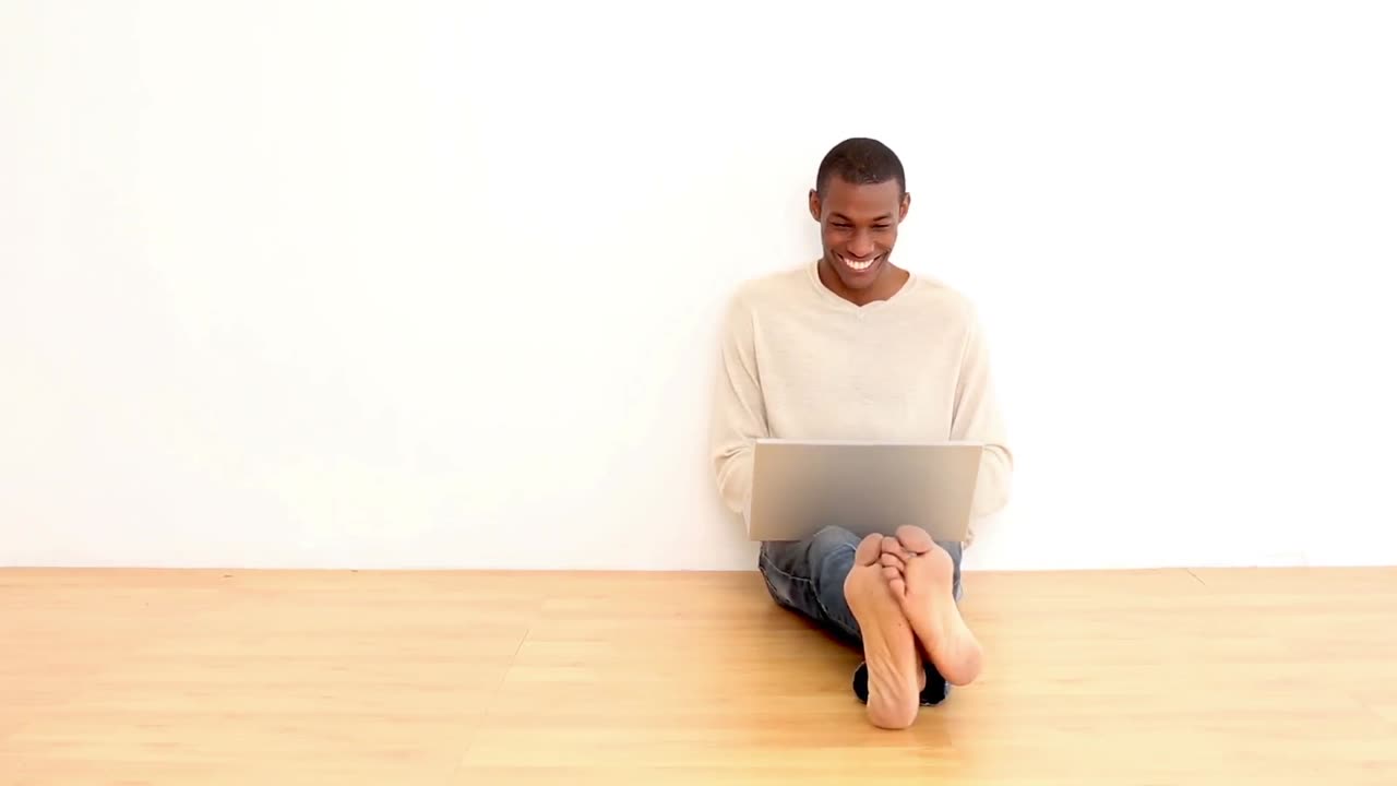 Smiling man using laptop sitting on the floor