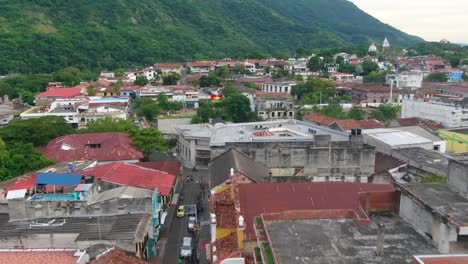 Aerial-flythrough-cathedral-towers-over-bustling-central-america-city-by-mountains