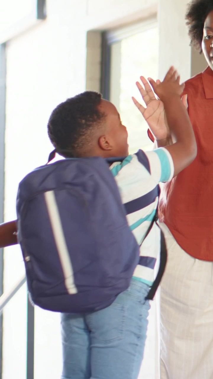 Reaching striped child with navy pack high-fiving parent in rust shirt entering entryway to leave