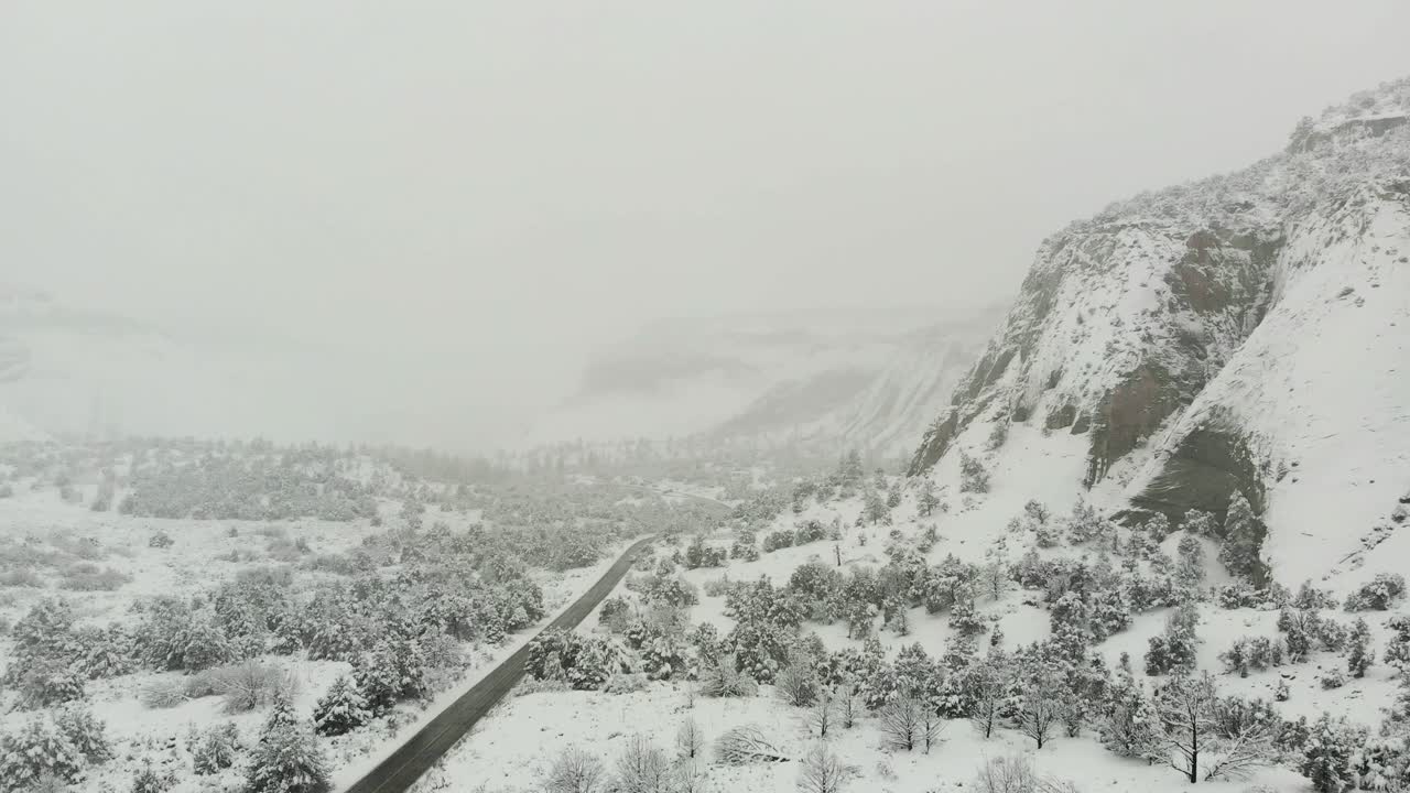 Aerial shot of a beautiful snow covered road with mountains buried in the fog.