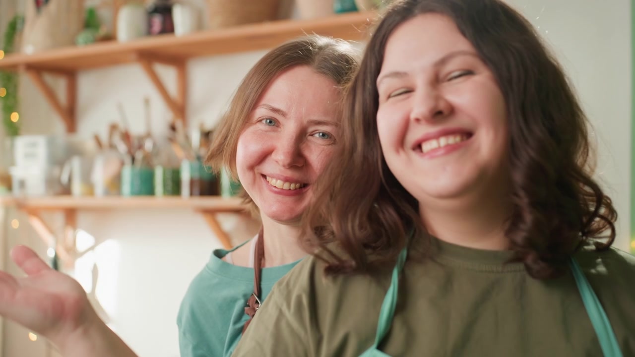 To keramikere smiler efter brændingsprocessen. Pottemagere fejrer succes med strålende smil. To kunsthåndværkere i et solbeskinnet studie deler muntert et sejrrigt og venligt øjeblik efter brændingen
