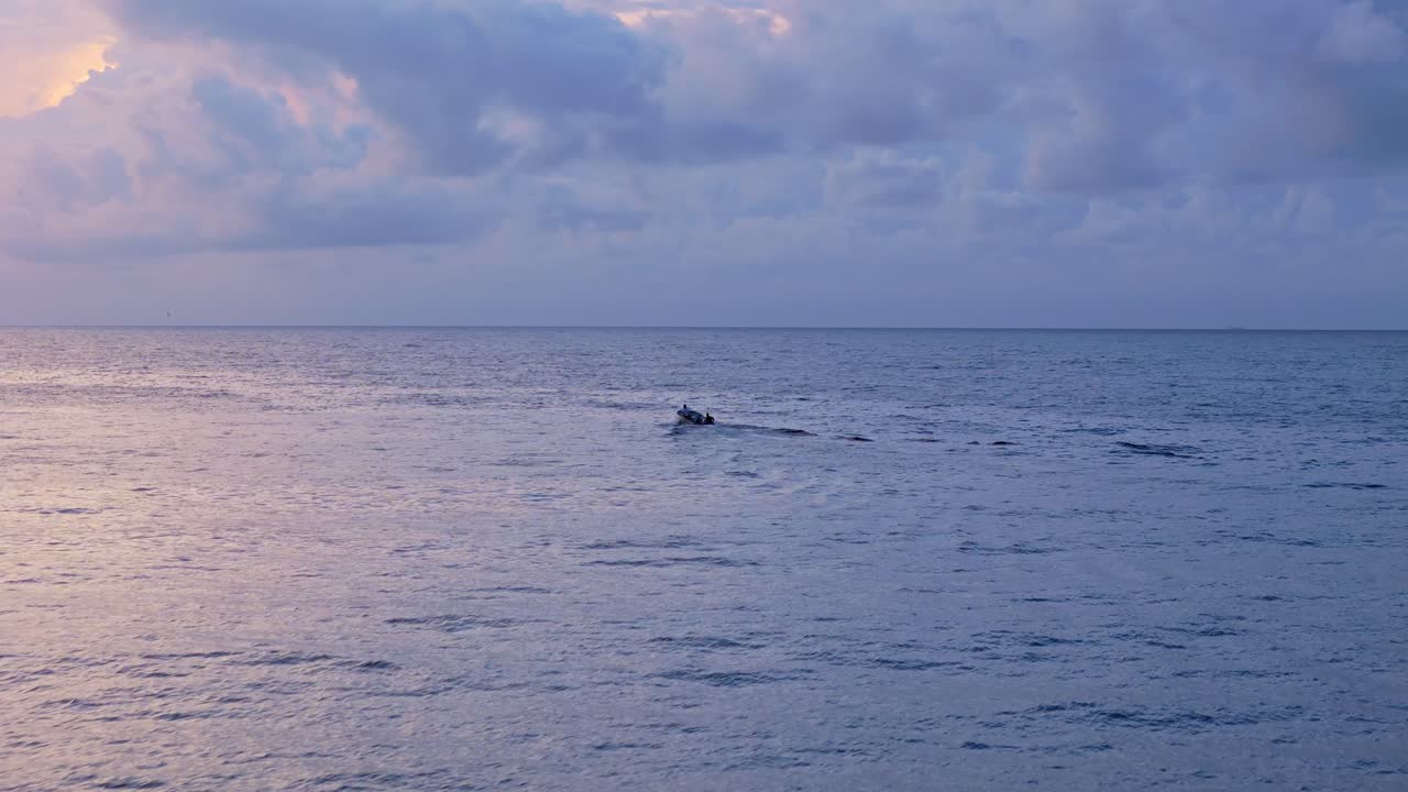 Angled rear view of small fishing boat driving bobbing in open ocean under blue hour cloudy sky
