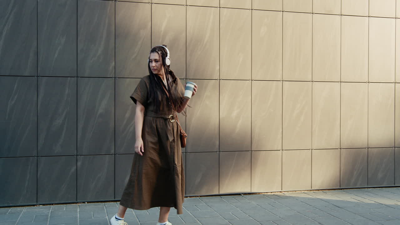 mujer caminando por la ciudad con auriculares y café