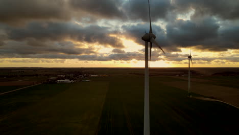 aerial view showing silhouette of rotating windmills in front of cloudy sunset in backdrop