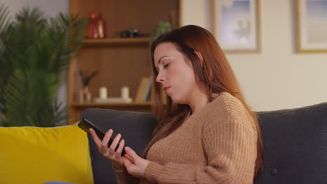 Woman-Sitting-On-Sofa-At-Home-At-Streaming-Or-Watching-Movie-Or-Show-Or-Scrolling-Internet-On-Mobile-Phone-4