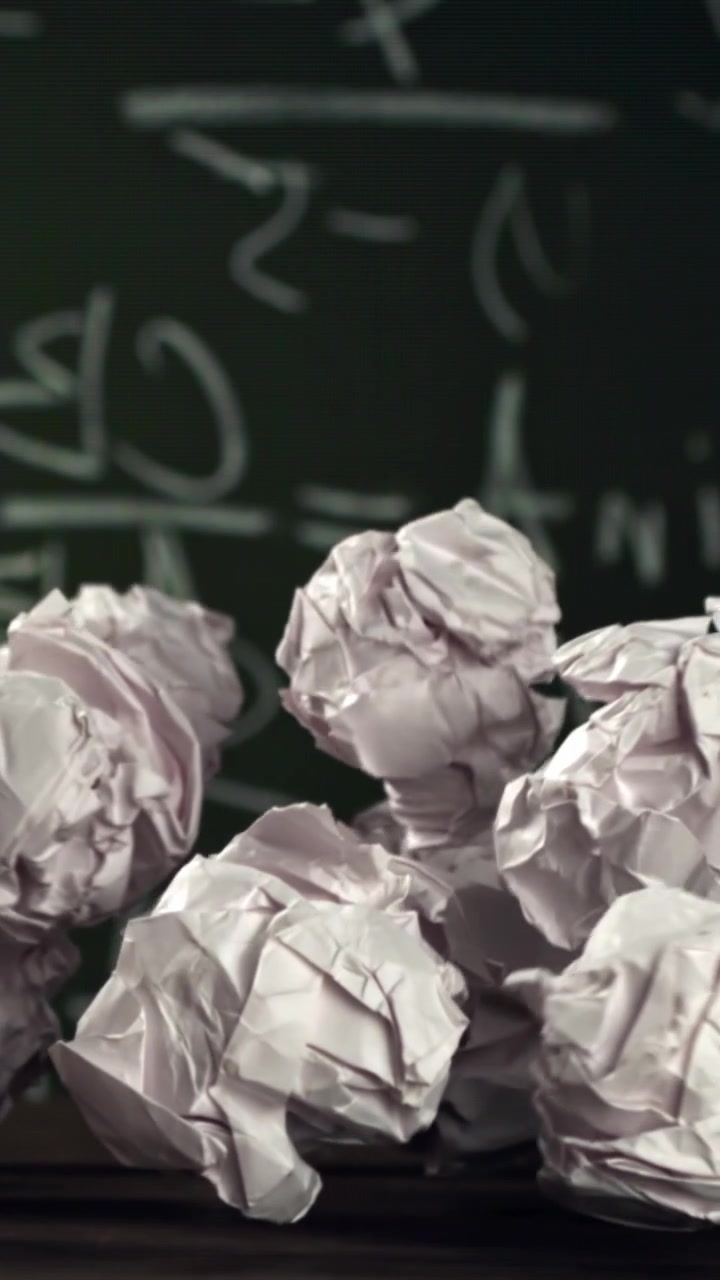 Crumpled Paper Balls Falling in Slow Motion Against a Chalkboard with Math Equations