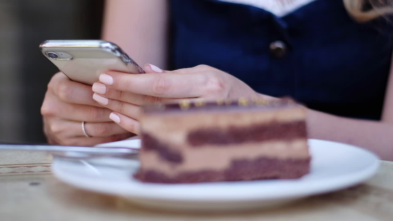Close up of a woman scrolling on her phone with a piece of chocolate on the table at a restaurant