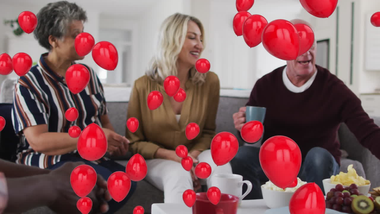 Múltiples globos rojos flotando sobre dos parejas mayores diversas desayunando juntos en casa.