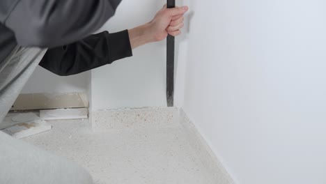 Hand-of-white-man-removing-tile-skirting-with-pry-bar-and-hammer