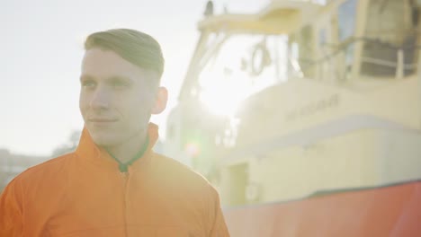 Harbor-master-in-orange-uniform-standing-in-front-of-a-large-ship-in-harbour-and-smiling