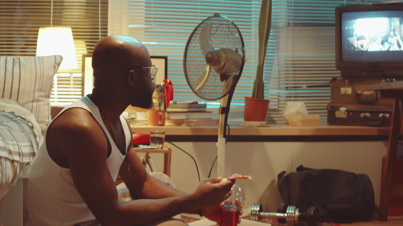 African American Man Watching TV and Eating Pizza in Evening at Home