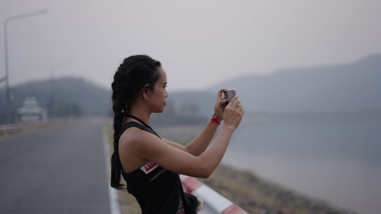 Woman taking photos of a scenic lake and mountain landscape with her smartphone