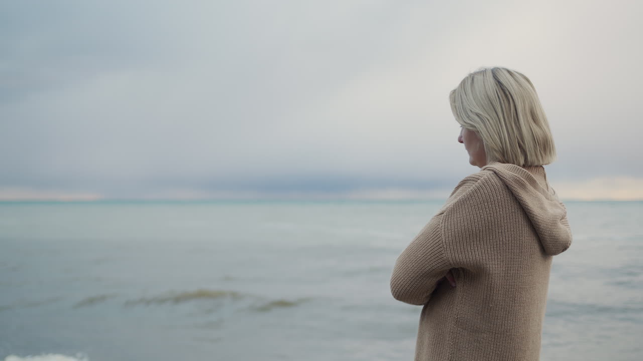 A woman in a warm knitted sweater looks at the sea where the storm begins