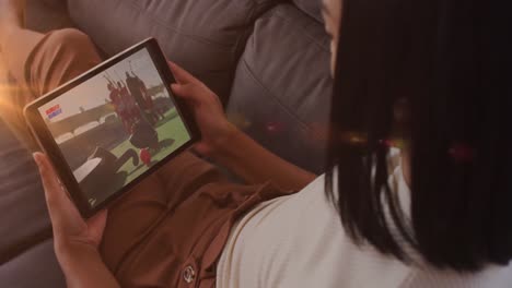 animation of glowing lights over biracial woman watching football on tablet