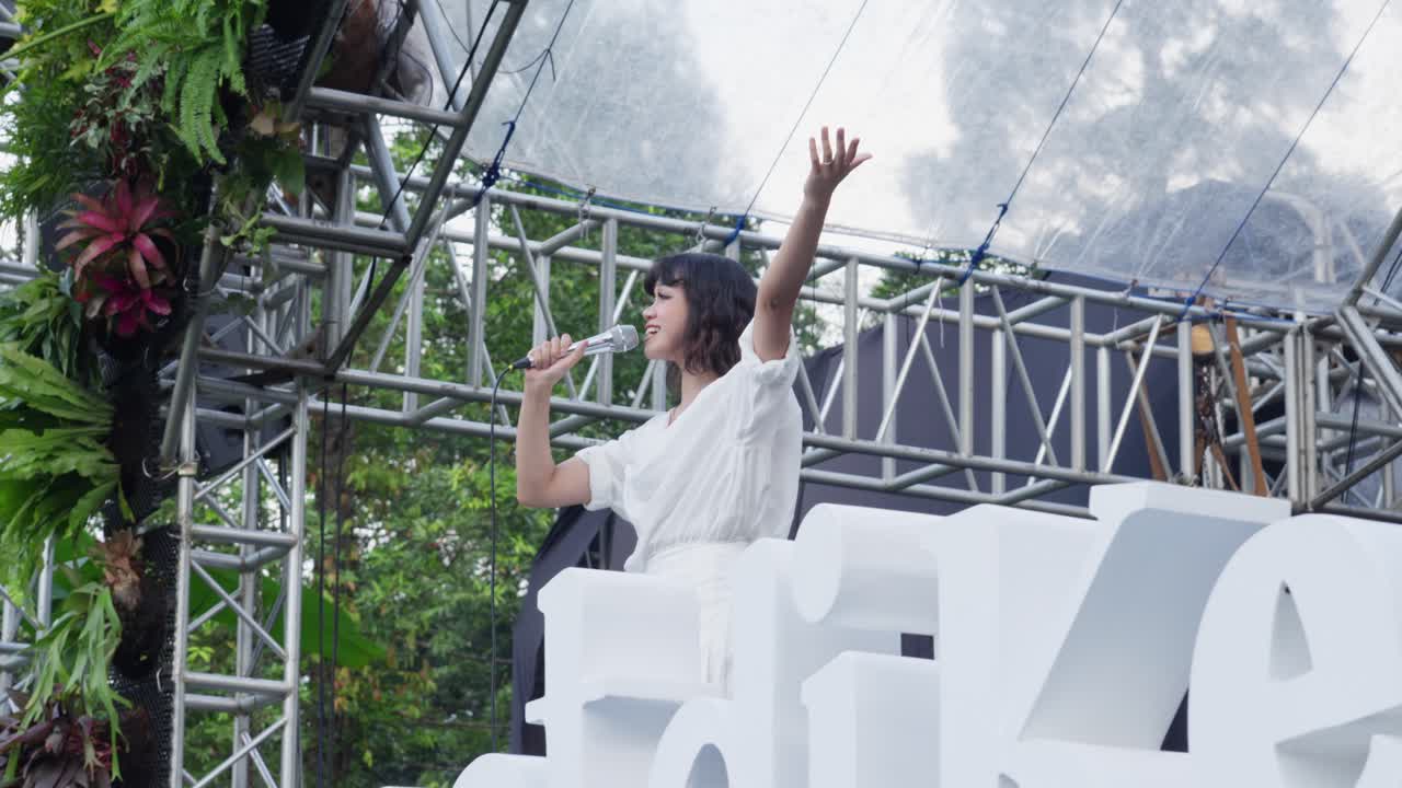 Female Member Of Indonesian Band Singing On Stage At Sunset In Bogor Botanical Gardens Event In Indonesia. low angle shot