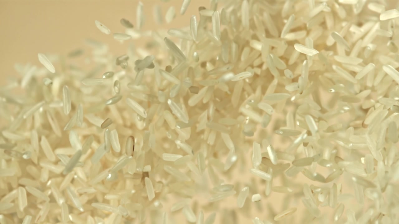Chicchi di riso bianco che cadono al rallentatore su uno sfondo beige