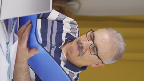 Vertical-video-of-Home-office-worker-old-man-reviewing-paperwork-files.